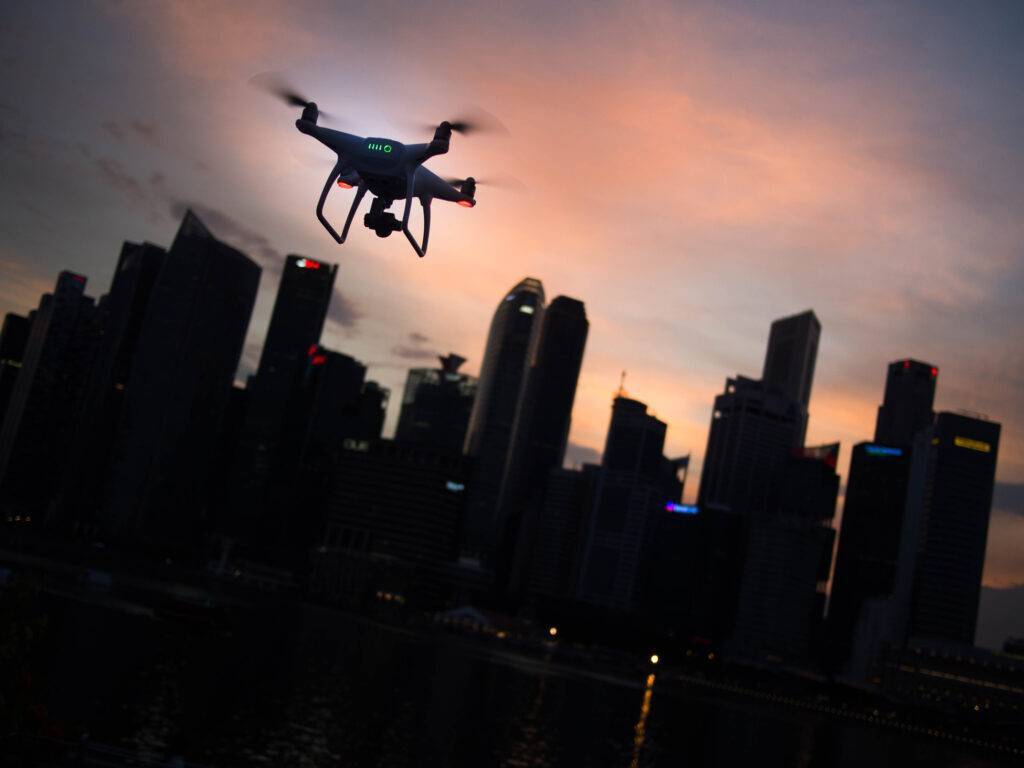 A drone flying in a city near a skyline at dusk.